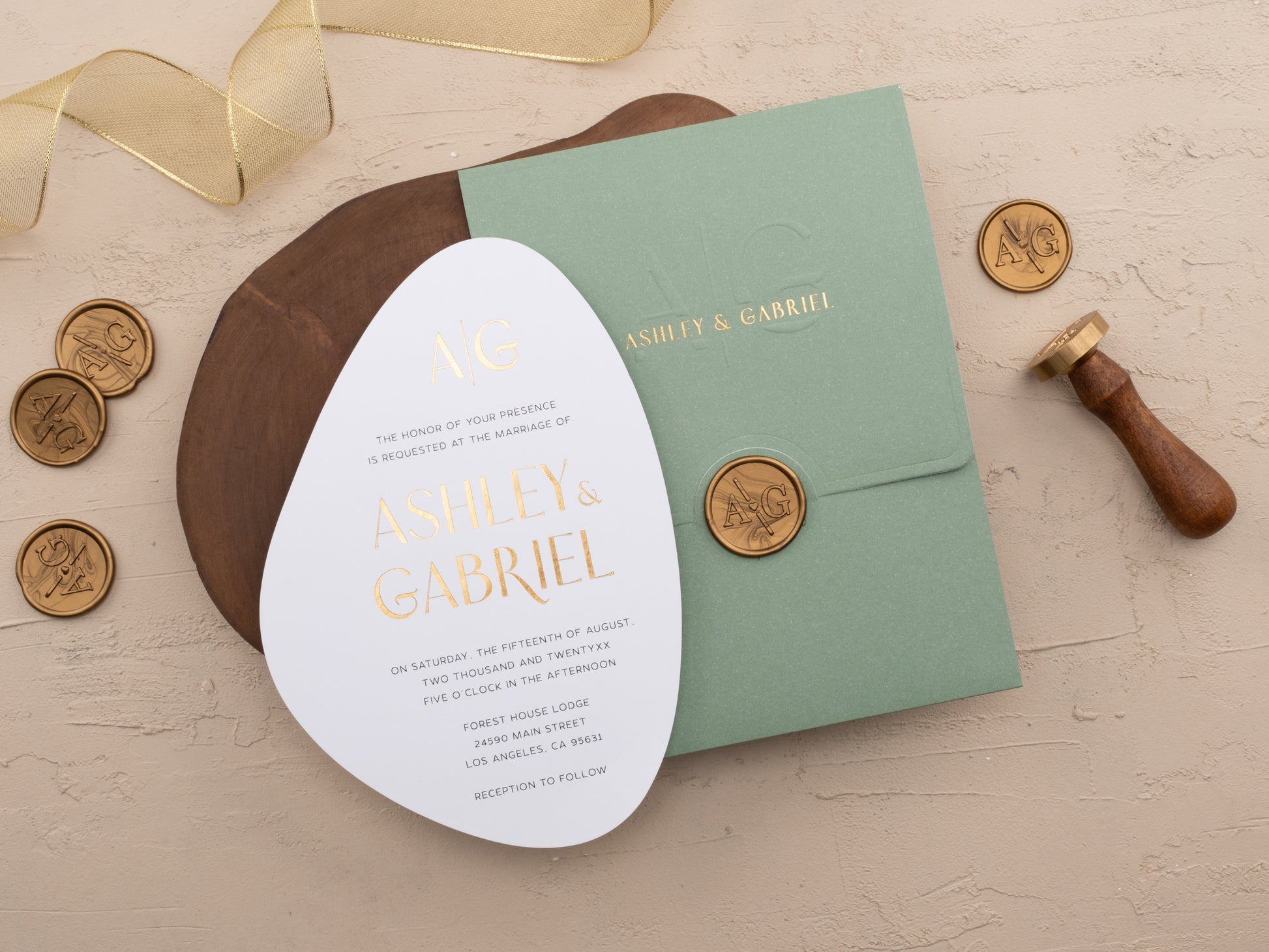 Elegant oval invitation in white with gold foil lettering next to soft green envelope