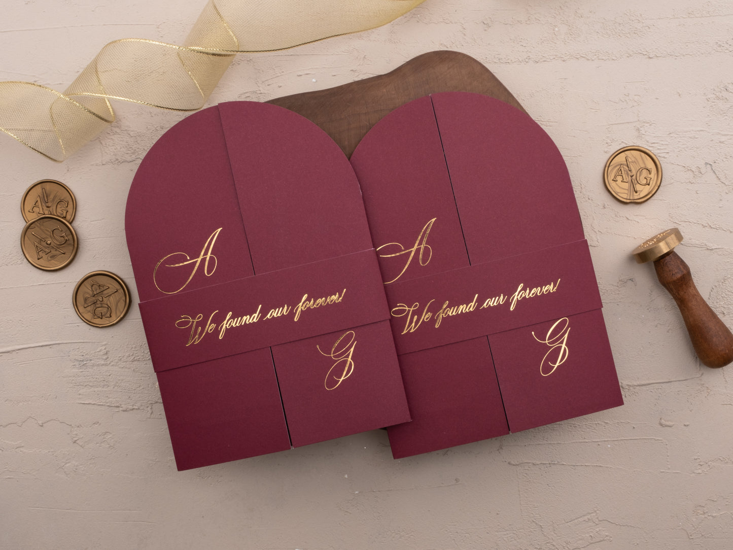 Closed burgundy invitation with gold belly band and initials