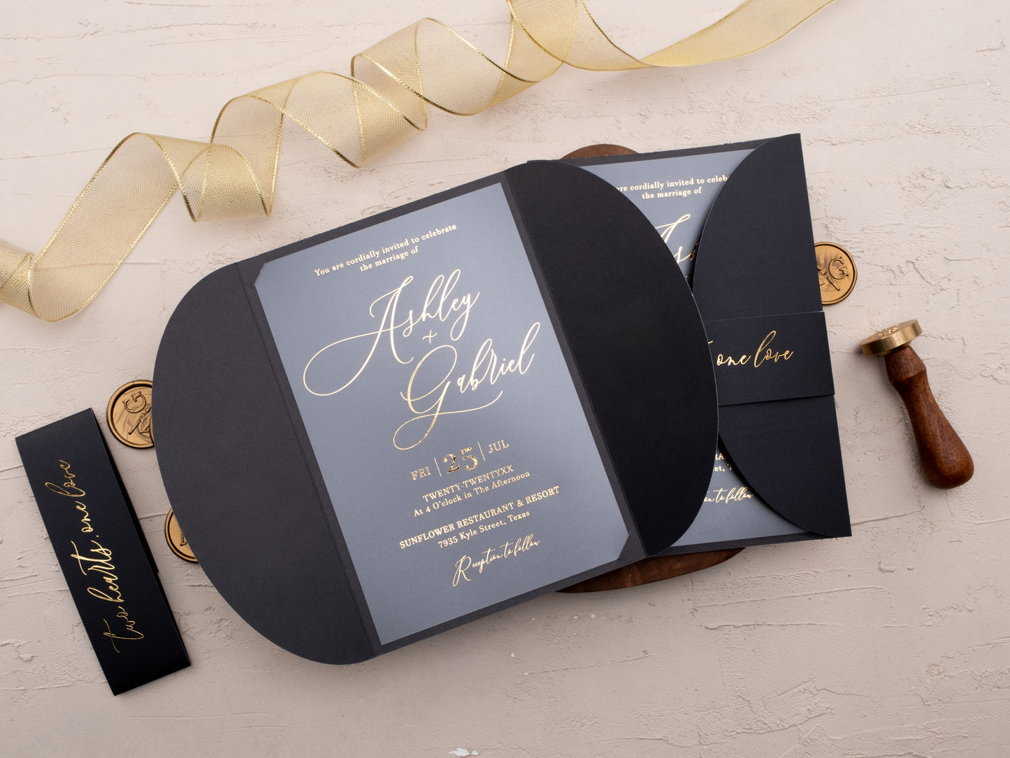 Black acrylic wedding invitation with gold foil on table with ribbon and wax seals