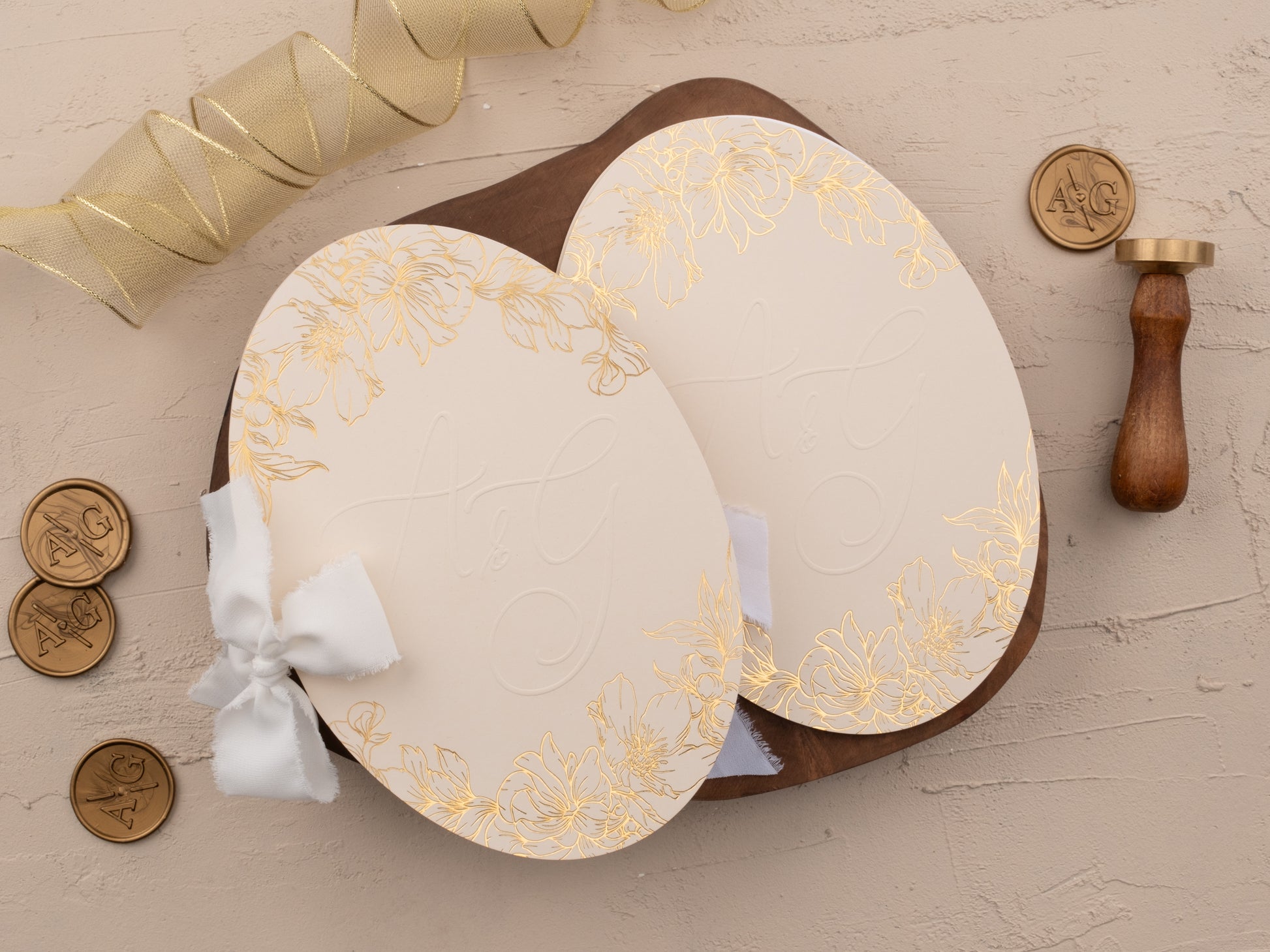 Ivory oval wedding invitation suite with gold foil and floral jacket, styled on beige background