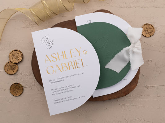 Emerald green wedding invitation with gold foil text, oval layout, and white ribbon, shown with matching embossed cover