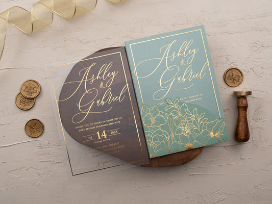 Sage green acrylic wedding invitation with gold foil floral design and matching sage envelope sleeve displayed on neutral textured background